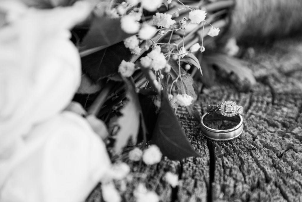 white roses sitting next to wedding rings on a wooden stump