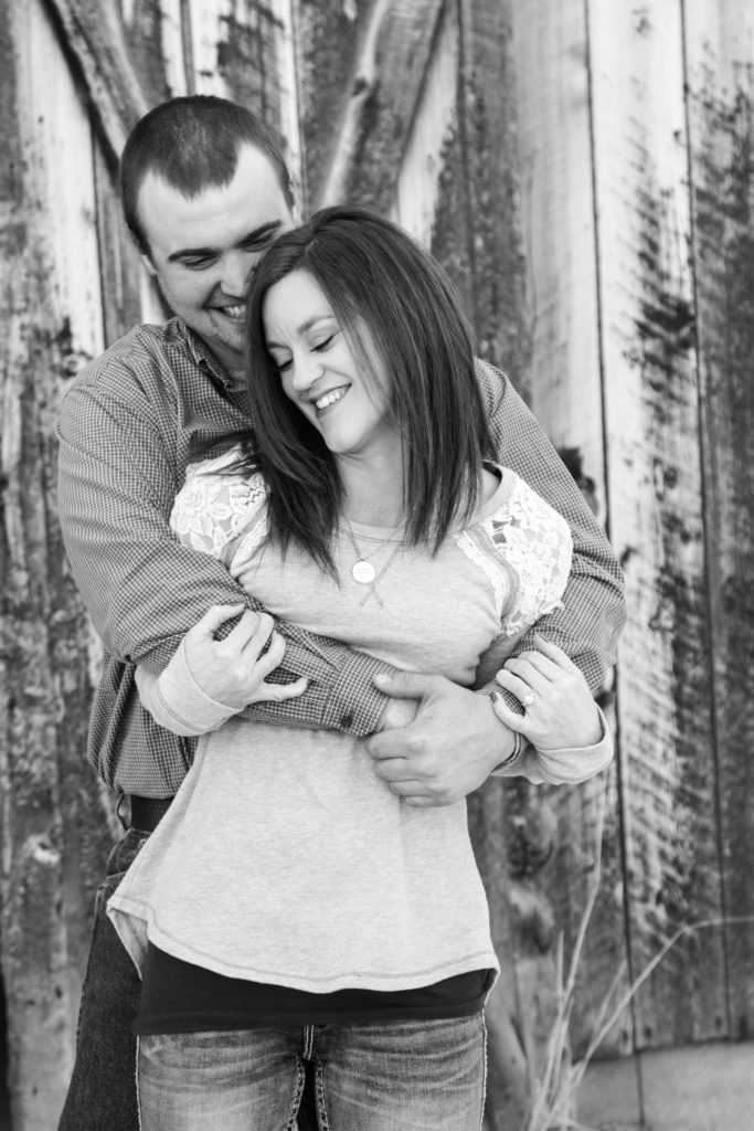 couple snuggling in front of barn door