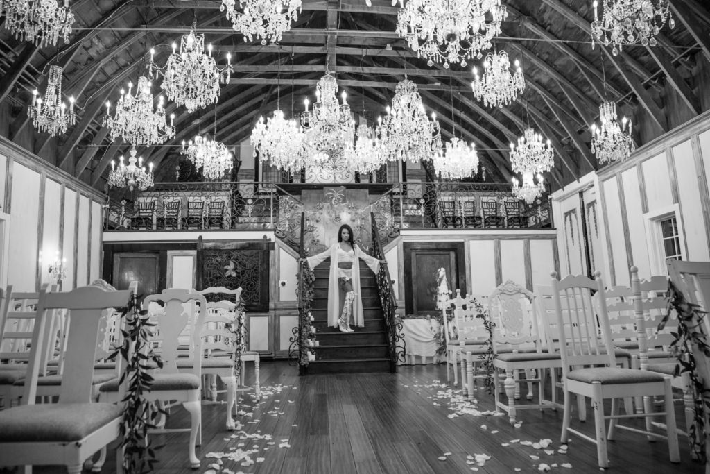 model in lingere on stairs in a barn filled with chandeliers