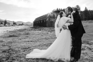 Bride and groom kissing in front of an old barn at sunset
