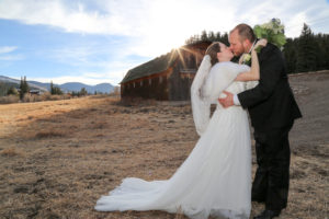 bride kissing groom by a barn at sunset