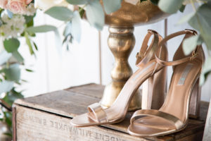 Rose gold high heels on wooden box next to flowers