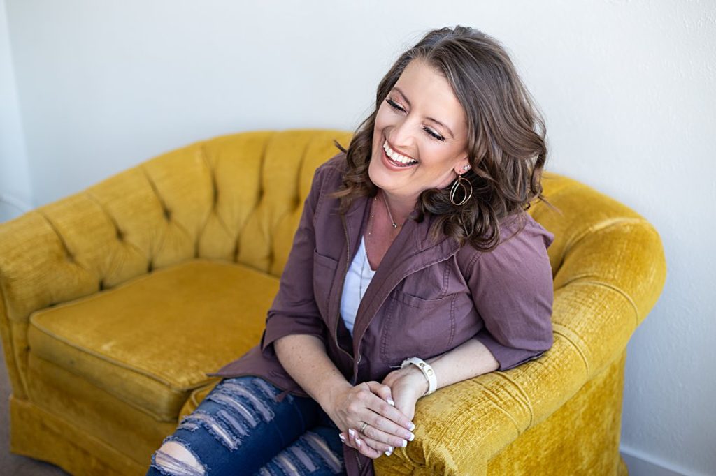 photographer Ashlee Bratton laughing on a gold couch 